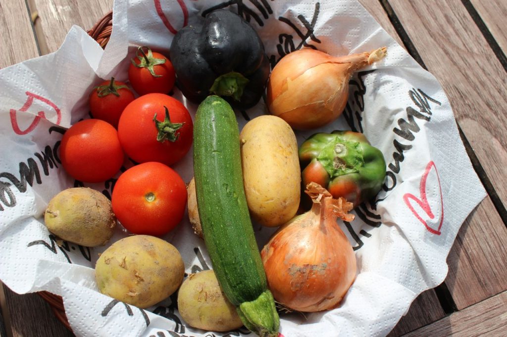 Top view of fresh organic vegetables including tomatoes, onion, and zucchini in a basket.