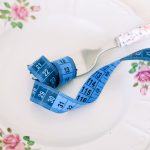 A floral plate with a fork and blue measuring tape symbolizing dieting or healthy eating.