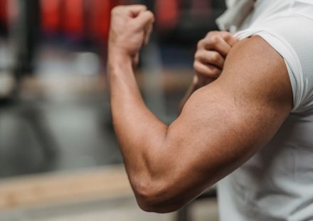 Crop anonymous sportsman in white shirt demonstrating biceps while training in modern gym