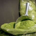 Close-up of fresh moringa powder in a stainless steel scoop, highlighting its vibrant green color.