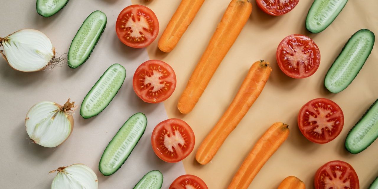Top view of fresh sliced vegetables including carrots, cucumbers, onions, and tomatoes in a flat lay design.