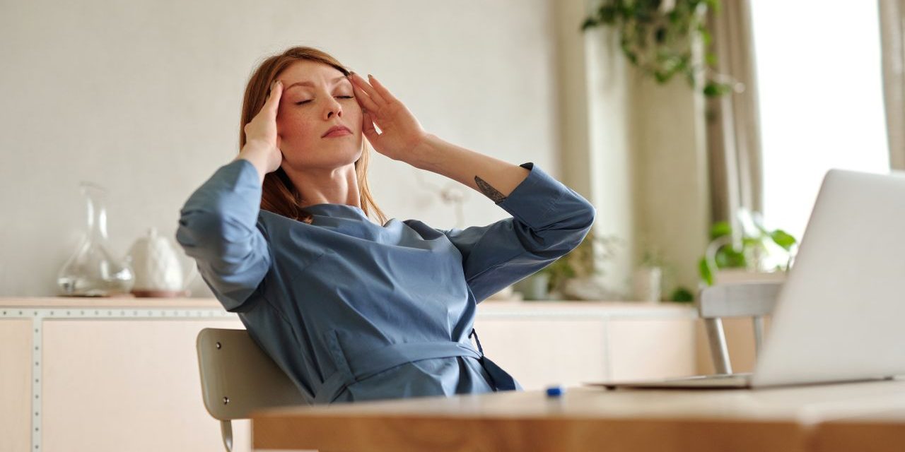 Woman experiencing stress at work, sitting at desk with a laptop, indoors.